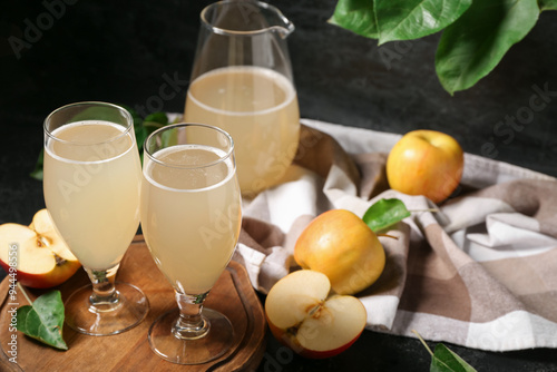 Glasses and jug of fresh apple kvass on black background photo