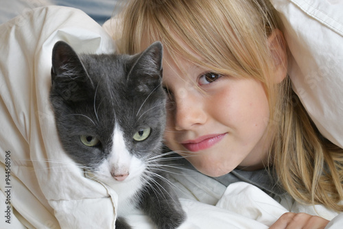 Little cute girl with a gray cat hid under a white blanket. photo