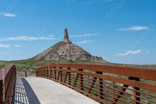 View of Chimney Rock from the bridge on a sunny day in Nebraska with clear blue skies and a hint of greenery