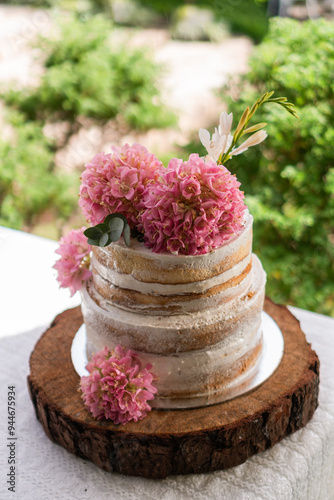 A wedding cake with pink flowers on top is sitting on a wooden base photo