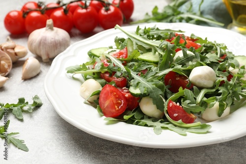 Tasty salad with arugula, mozzarella, tomatoes and cucumber on grey textured table, closeup