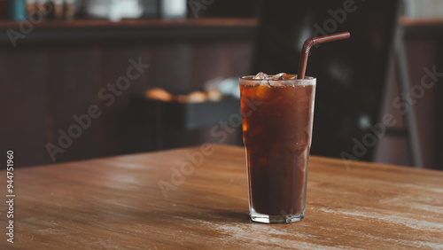 Ice americano coffee in a tall glass with ice cubes on a wood table. Cold summer drink with tubes on a table Black Russian Cocktail with Vodka and Coffee Liquor.