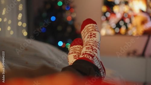 Cozy holiday scene with feet in red and white snowflake socks stretched out in front of colorful bokeh lights, evoking a warm, festive atmosphere.