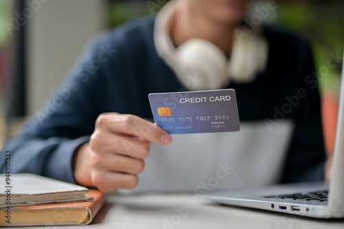 A close-up image of a man holding a credit card over a table while using his laptop.