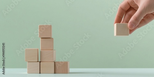 A hand placing a wooden block on top of other blocks, symbolizing creativity and construction.