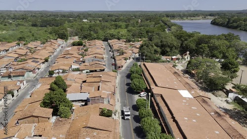 Drone flies to left over road cutting through neighborhood next to river and houses with orange tile roofs photo