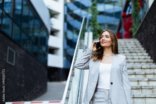 Professional woman smiles while checking her smartphone as she walks down sleek urban steps during a sunny afternoon in the city