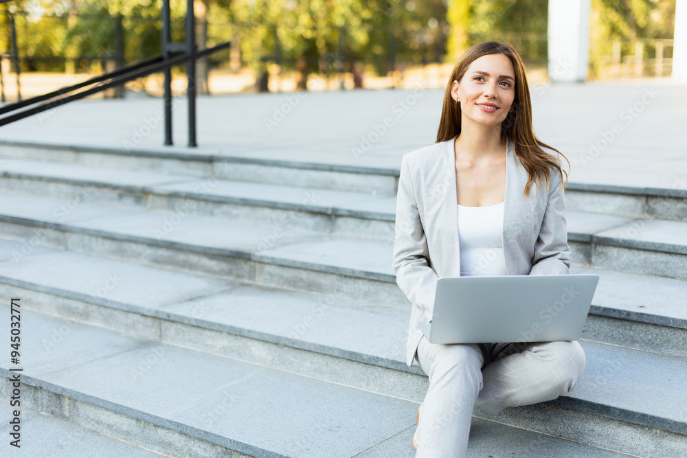 Stylish professional woman working on her laptop while seated on modern outdoor steps in a bustling urban setting during the golden hour Stylish professional woman working on her laptop while seated on modern outdoor steps in a bustling urban setting during the golden hour