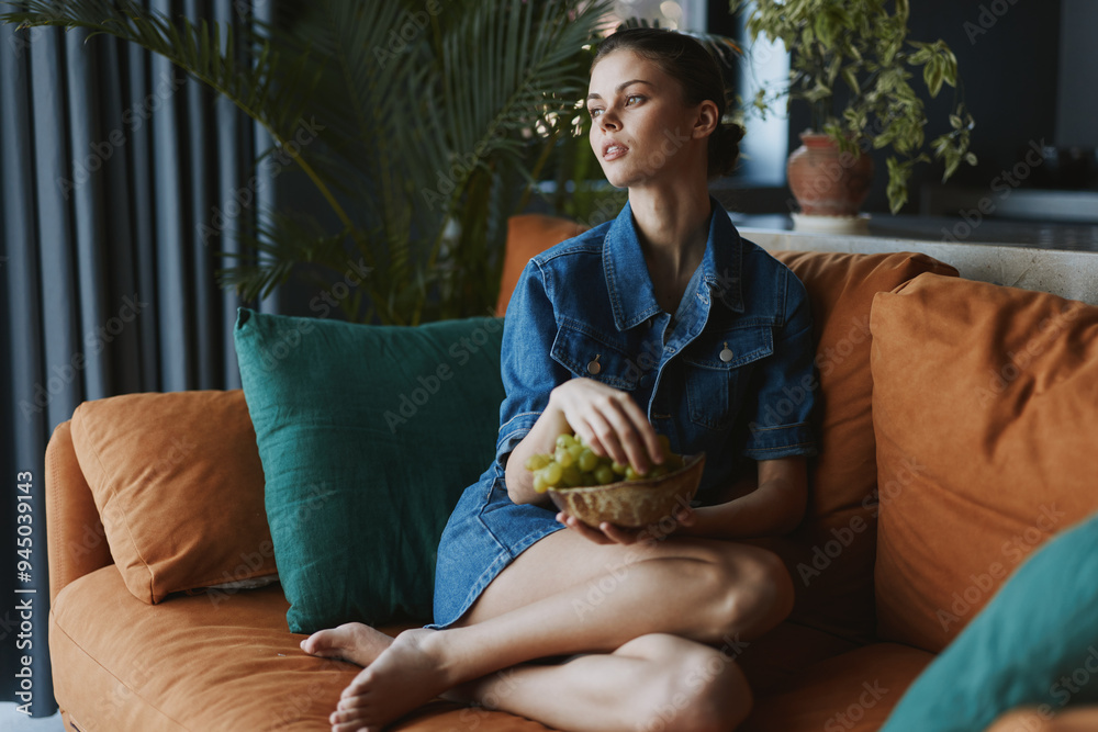 Obraz premium Woman Relaxing on Orange Couch with Basket of Grapes in Front of Her in Cozy Living Room Setting