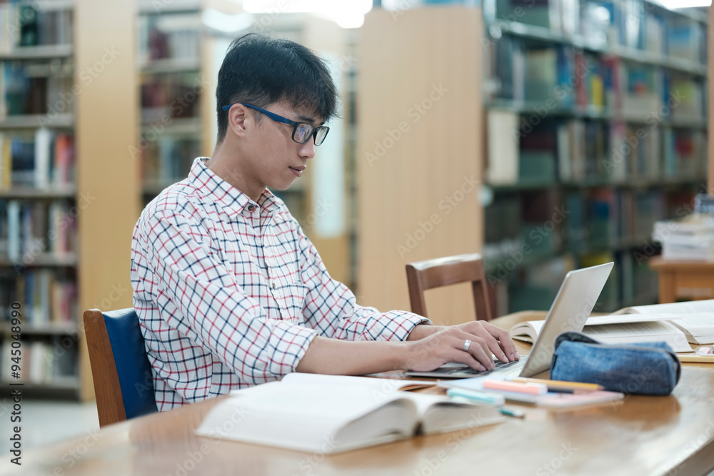 Young Asian male sitting inside a library alone doing research. Man working on a project. Young man doing research for a case. Young Asian male sitting inside a library alone doing research. Man working on a project. Young man doing research for a case.