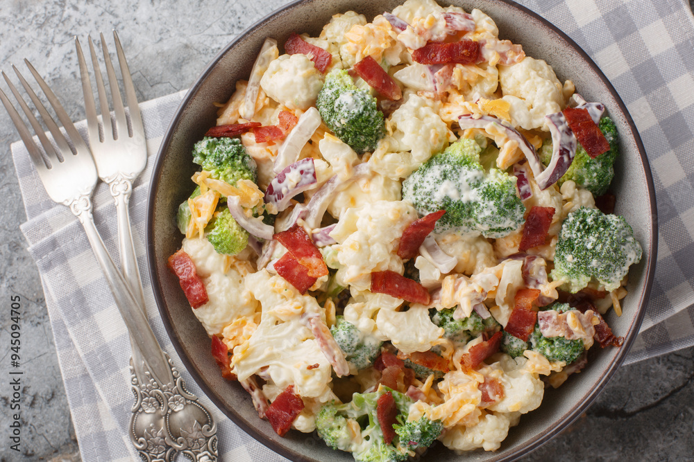 Salad with cauliflower, broccoli, cooked bacon, cheese and red onion closeup on the bowl on the table. Horizontal top view from above Salad with cauliflower, broccoli, cooked bacon, cheese and red onion closeup on the bowl on the table. Horizontal top view from above