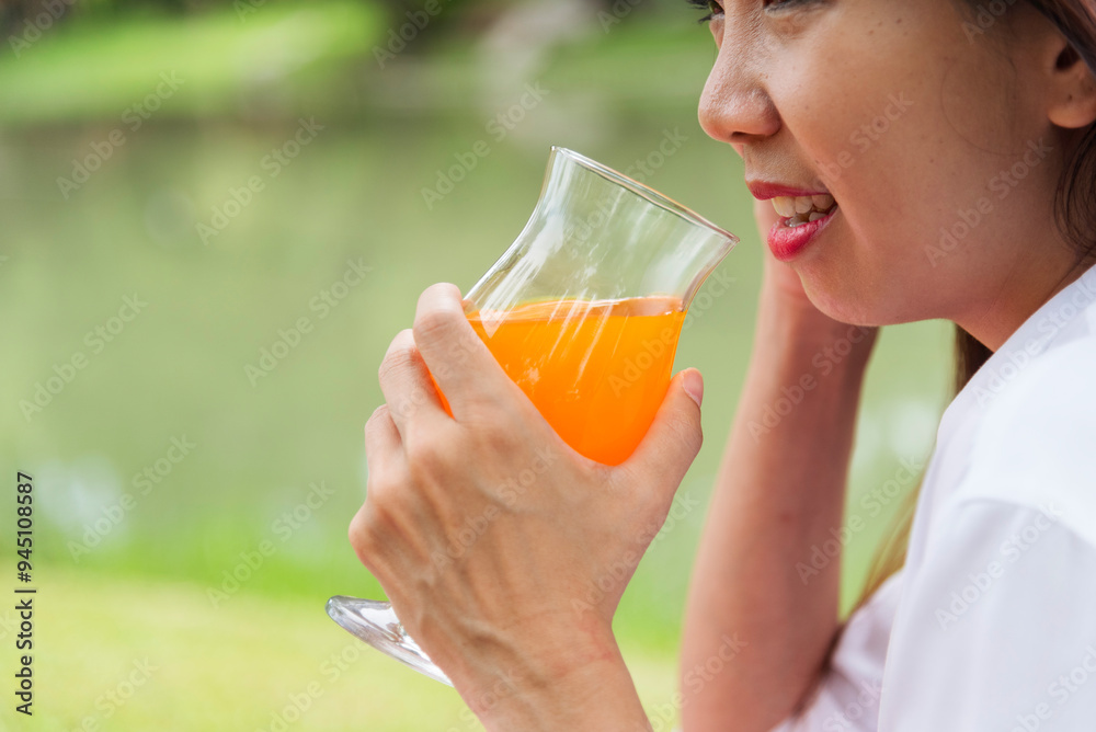 Women hands drink orange juice fresh fruit cool drinking in green park garden. Asian women hands holding healthy drinking glass. Beautiful female pouring orange juice from cocktail bottle outdoors