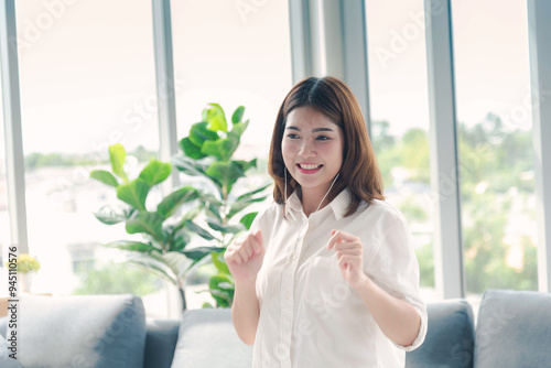 Happy asian dancing woman use headphones listen to music from smartphone happy dance in living room at home. Music mental therapist relaxation woman. Cheerful wellness women dance exercise wellbeing