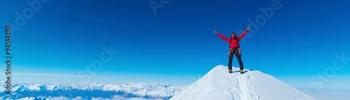 A climber celebrates reaching the summit of a snowy mountain under a clear blue sky.