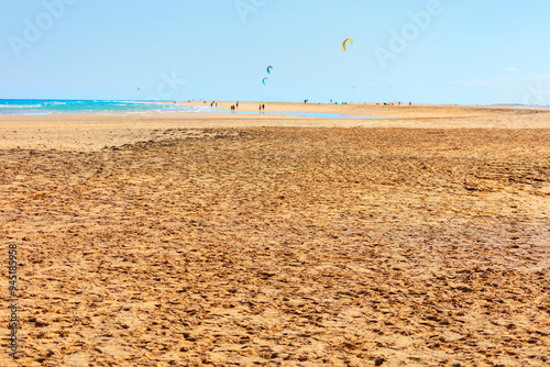  Sandy beach with a few people and a kite flying in the sky. Sunny beach, with waves gently crashing in the background