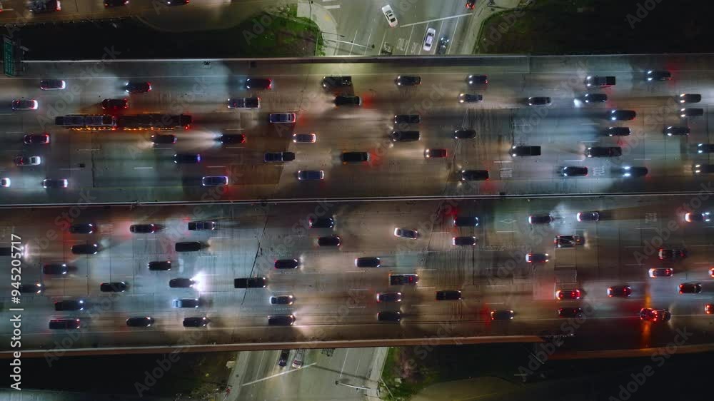 An aerial night view reveals the busy traffic congestion in downtown Los Angeles, with city lights and rows of vehicles creating a bustling scene below, showcasing the urban hustle and bustle