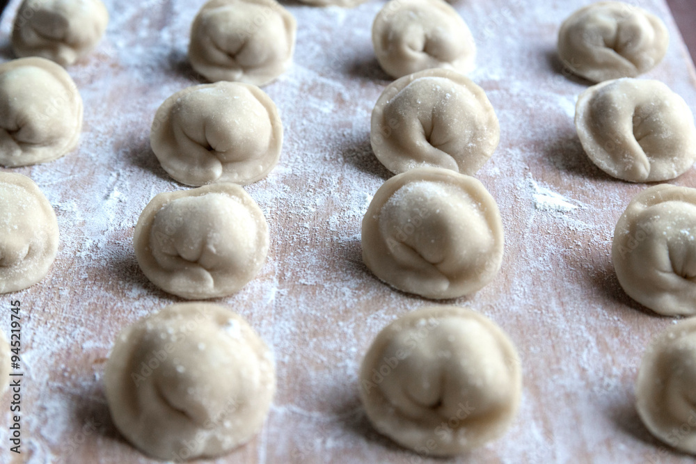 The raw dumplings were placed on a wooden cooking board, sprinkled with flour. The filling is minced meat, potatoes, cheese or cottage cheese. A semi-finished product, ready for cooking. The raw dumplings were placed on a wooden cooking board, sprinkled with flour. The filling is minced meat, potatoes, cheese or cottage cheese. A semi-finished product, ready for cooking.