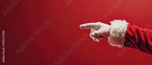 Santa Claus's white-gloved hand pointing to the left against a solid red background. The arm is clad in the red sleeve with white fur trim as part of Santa's iconic outfit. Generative AI photo