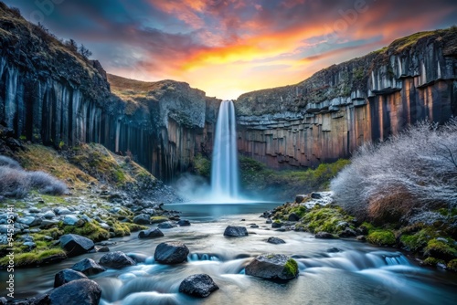 Moody misty dawn silhouette of Svartifoss waterfall against soft pastel blue sky with delicate frosty foliage and subtle morning dew droplets. photo