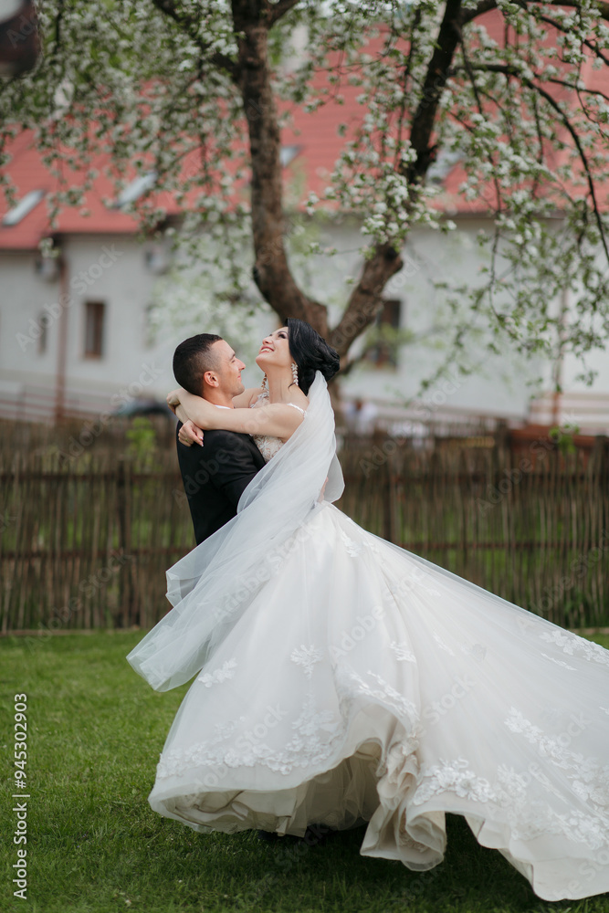 A bride and groom are standing in a field with a red roof in the background. The bride is wearing a white dress and the groom is wearing a black suit. They are both smiling and hugging each other A bride and groom are standing in a field with a red roof in the background. The bride is wearing a white dress and the groom is wearing a black suit. They are both smiling and hugging each other