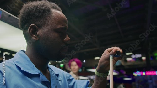 Chest up of young African American man calking his cue while playing billiards in bar at night photo