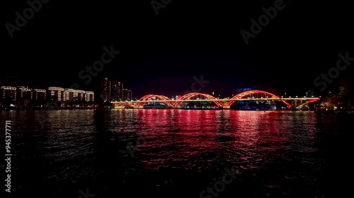 A stunning night scene of Wenhui Bridge in Liuzhou, Guangxi, China, illuminated with vibrant red lights, spanning over Liujiang River, creating a captivating reflection on the calm water below.  photo