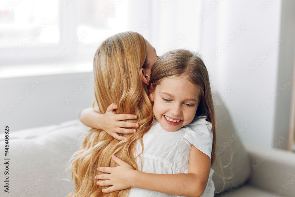 Two young sisters sharing a heartfelt hug while sitting on a cozy couch by a sunlit window