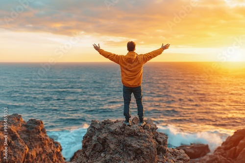 Man Standing on Cliff Top With Arms Raised at Sunset.