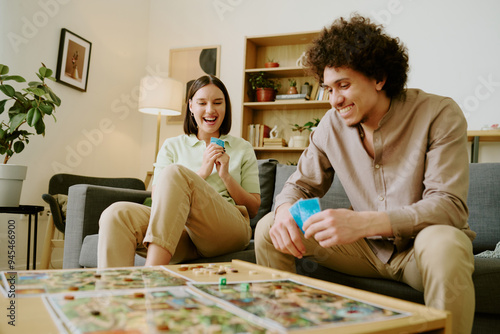 Canvas Print Joyful young biracial couple having fun playing modern fantasy board game in liv