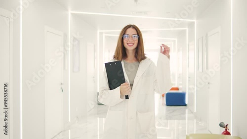 Smiling female family doctor with tablet looking at camera in modern hospital corridor