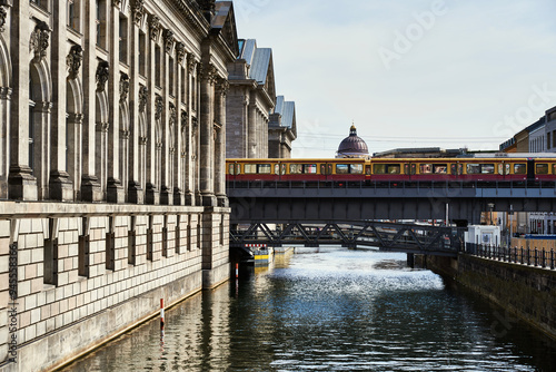 Yellow metro in Berlin stopped over a bridge on the river Spree with the castle dome standing out. Historical old building by the canal with the subway standing by on a bridge. Berlin tourism concept