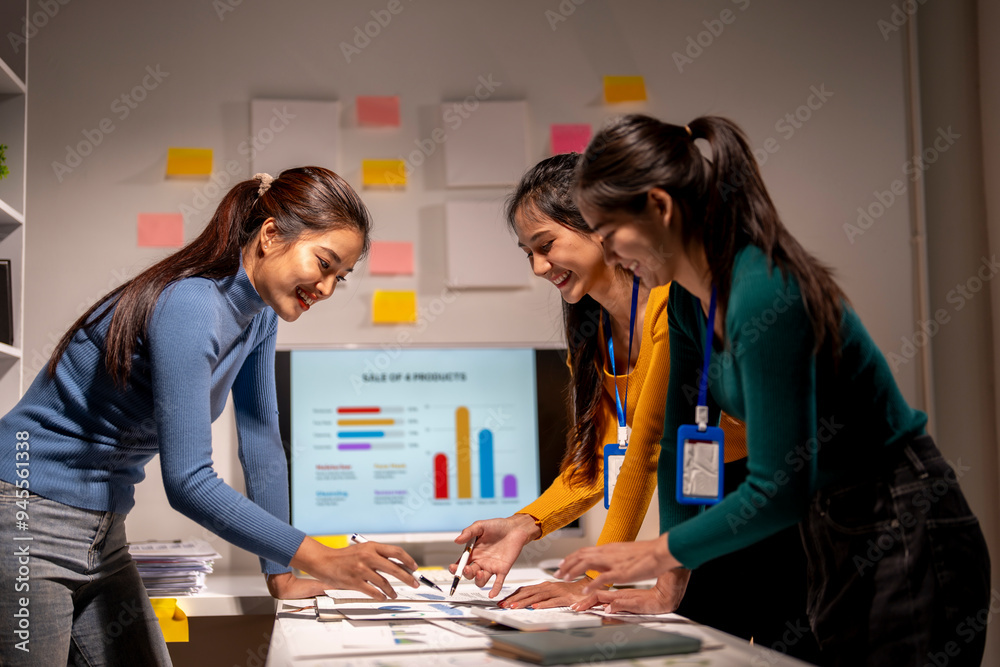 Fototapeta premium Three women are sitting at a table with a computer monitor in front of them