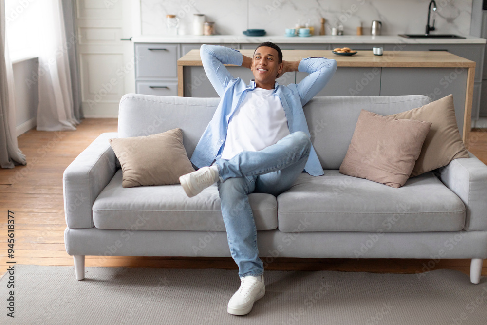 Rested black man sitting on comfortable couch at home, leaning back with hands behind head, enjoying weekend or break from work Rested black man sitting on comfortable couch at home, leaning back with hands behind head, enjoying weekend or break from work