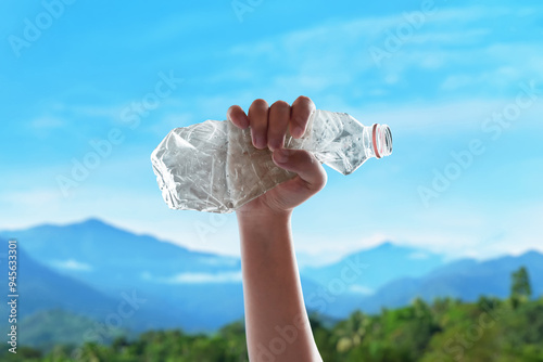 Closeup of hand holding empty plastic bottle on the streeet with blue sky photo