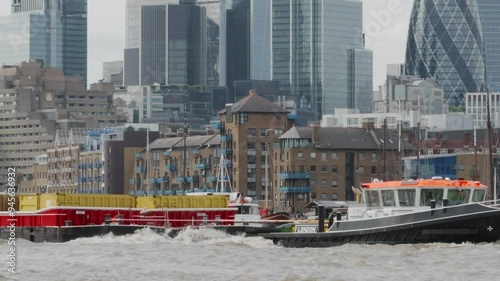 River Thames boat traffic.
A tug pulling barges on the Thames with City towers in the background.
 photo