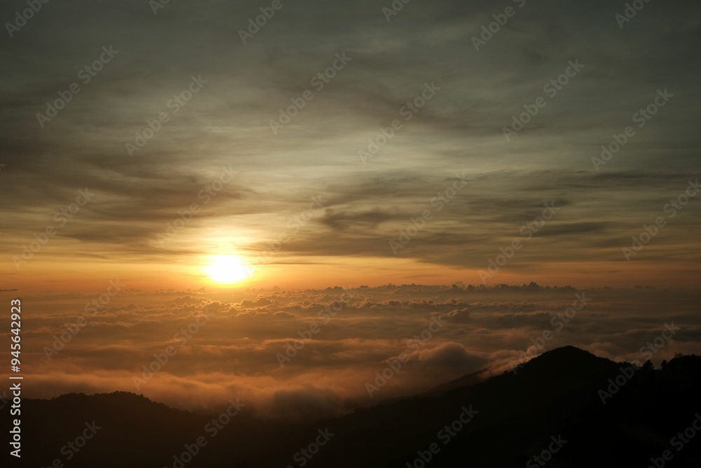 Sunrise over the mountains. Warm colors over a sea of clouds with silhouette of mountains on the horizon. Sunrise over the mountains. Warm colors over a sea of clouds with silhouette of mountains on the horizon.