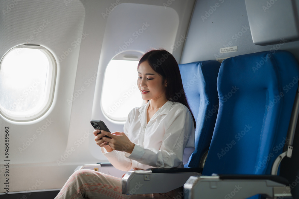 Woman Relaxing on Airplane: A serene young woman uses her smartphone while seated in a comfortable airplane seat, enjoying the view through the window. This image evokes a sense of travel, relaxation Woman Relaxing on Airplane: A serene young woman uses her smartphone while seated in a comfortable airplane seat, enjoying the view through the window. This image evokes a sense of travel, relaxation
