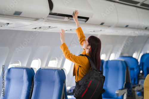 Ready for Takeoff: A young woman stows her luggage in the overhead compartment, embodying the excitement and anticipation of air travel. 