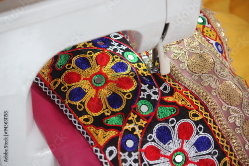 stitching machine closeup for sewing the floral design traditional navratri laces for chaniya choli. dress is getting ready by a tailor. stitching business for navratri festival in gujarat india.  photo