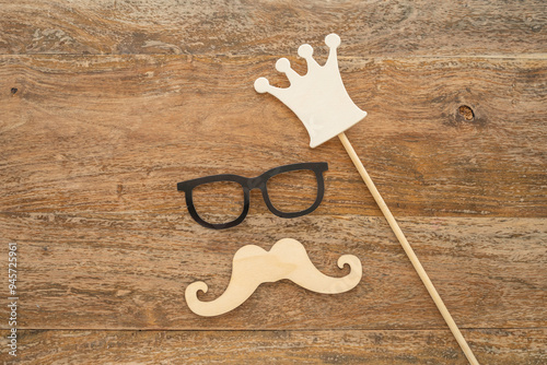 Father's Day concept with decorative moustache, glasses and crown over wooden background.