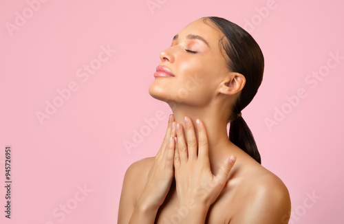 Attractive adorable serene young woman touching pure neck skin isolated over pink background, free space photo