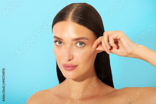 Skin firming concept. Beautiful young lady with flawless tight skin touching her cheek and looking at camera, posing over blue studio background photo