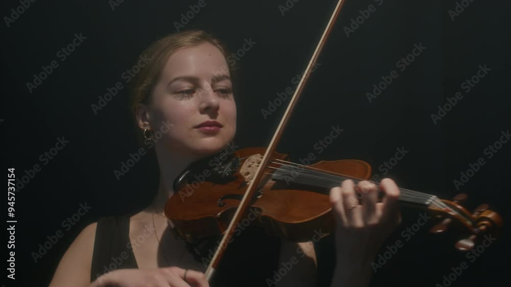 Medium shot of beautiful female violinist duo playing music on black background Medium shot of beautiful female violinist duo playing music on black background