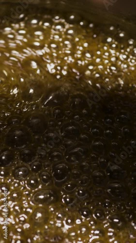 Close-up of melted boiling caramel being stirred with a spoon by a pastry chef while preparing homemade candies photo