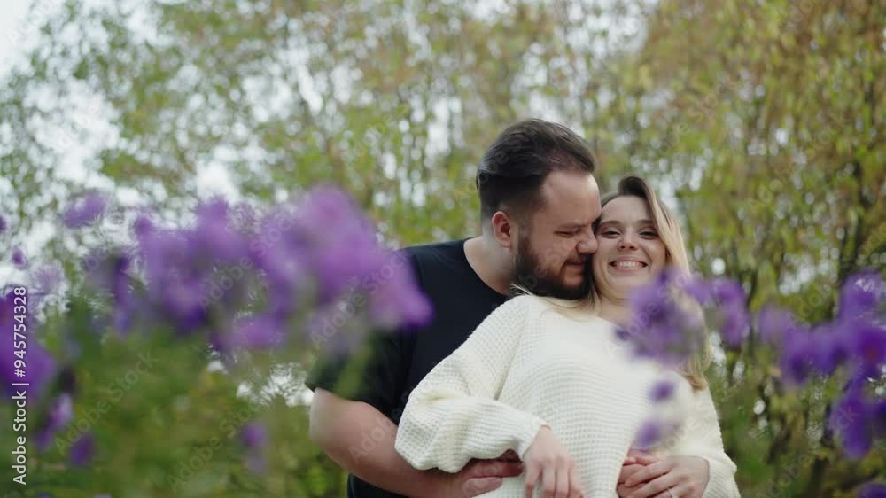 A beautiful young couple share a loving embrace in a lush garden, surrounded by vibrant purple flowers. This image captures a moment of genuine affection and joy, perfect for themes of love