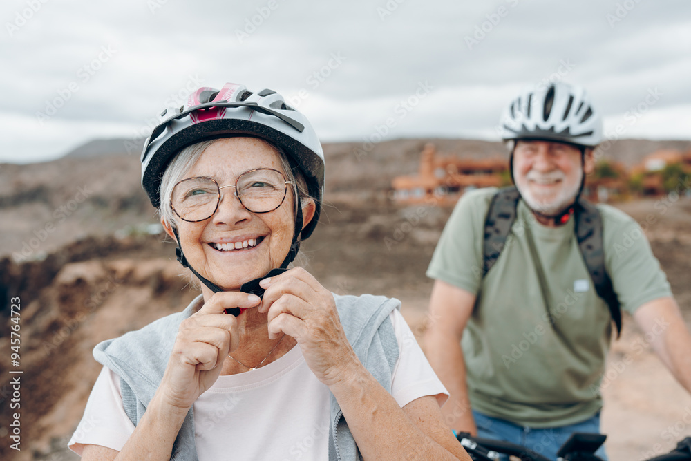 Portrait of one old woman smiling and enjoying nature outdoors riding bike with her husband laughing. Headshot of mature female with glasses feeling healthy. Senior putting on helmet to go trip Portrait of one old woman smiling and enjoying nature outdoors riding bike with her husband laughing. Headshot of mature female with glasses feeling healthy. Senior putting on helmet to go trip