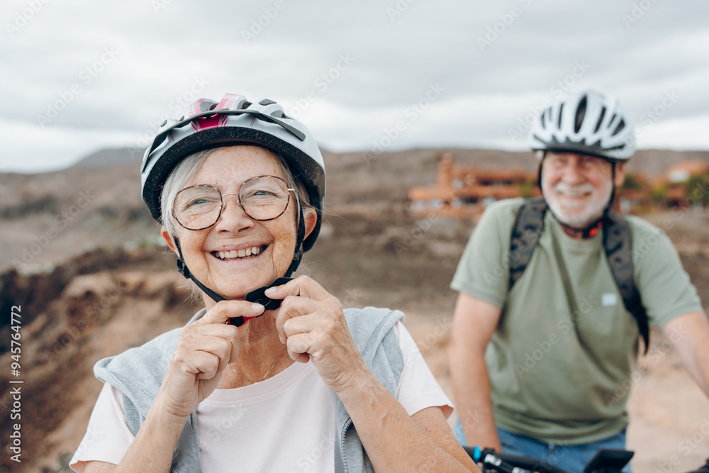 Portrait of one old woman smiling and enjoying nature outdoors riding bike with her husband laughing. Headshot of mature female with glasses feeling healthy. Senior putting on helmet to go trip Portrait of one old woman smiling and enjoying nature outdoors riding bike with her husband laughing. Headshot of mature female with glasses feeling healthy. Senior putting on helmet to go trip