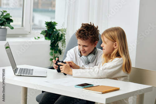 Happy Boy and Girl Studying Online with Laptops at Home Two Caucasian children, a boy and a girl, are sitting at a table in their cozy living room They are wearing headphones and concentrating on