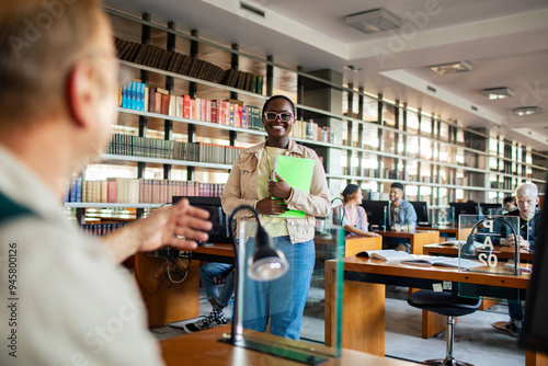 Smiling female black student returning paper to professor in college library