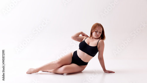 Uniqueness. Beautiful young woman with natural body posing in black underwear in floor isolated on white studio background. Concept of female beauty, body positivity, care, acceptance